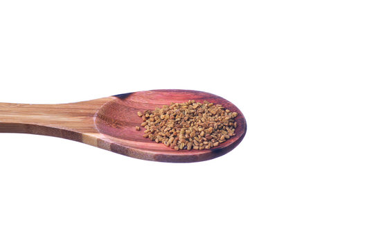 Fenugreek seeds on a brass spoon isolated on a white background.