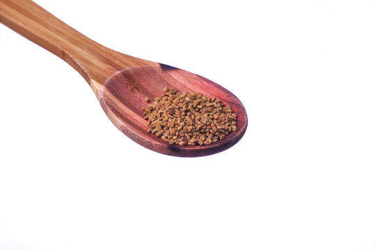 Fenugreek seeds on a brass spoon isolated on a white background.