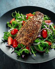 Smoked Mackerel Salad with tomato, chopped red onion, Ruccola on black plate.