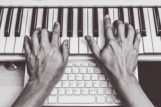 composer hands working on piano keys & computer keyboard. music production technology