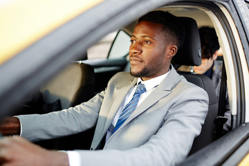 Portrait of successful African- American businessman driving car and focused on the road