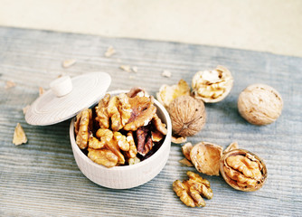 Walnut kernels in a wooden bowl and whole walnuts on old wooden table. Walnuts