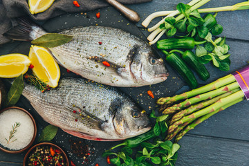 Delicious fresh fish on dark vintage background. Fish with aromatic herbs, spices and vegetables - healthy food, diet or cooking concept