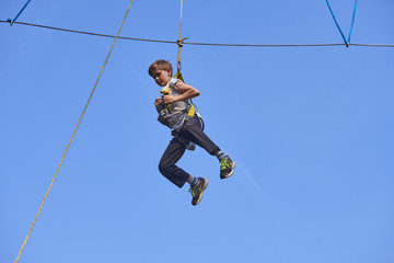 Cute school boy enjoying a sunny day in a climbing adventure activity park. Clear blue sky background. Children summer activities.