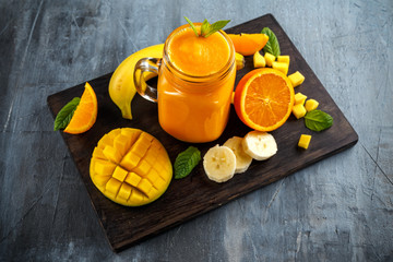 Fresh Orange smoothie drink with banana, mango on black wooden board.