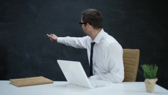 Businessman with laptop moving his hand as if underlining a word on chalkboard