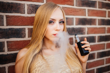 The sexy girl smoke electronic cigarette on the nature background. Vaping concept.
