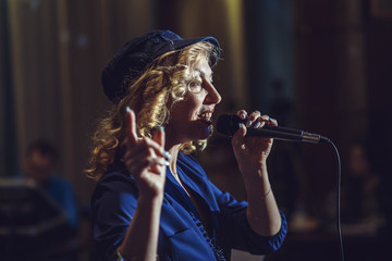 A female European singer sings into a microphone in a dark restaurant.