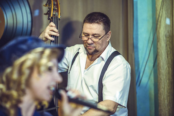 The vocal group performs at the restaurant. The singer and the man are playing the double bass.