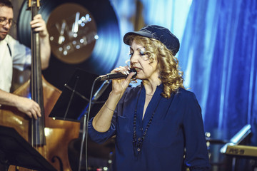 Concert in the restaurant. A middle-aged woman, of European appearance, sings into a microphone.