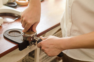 Close up of barista tamping fresh coffee for making espresso.