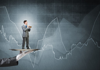 Young businessman on metal tray playing fife against concrete background with chart