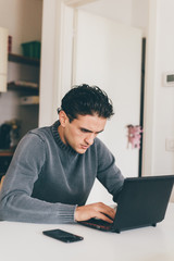Handsome young man sitting indoor using smart phone and computer - business, technology, internet concept