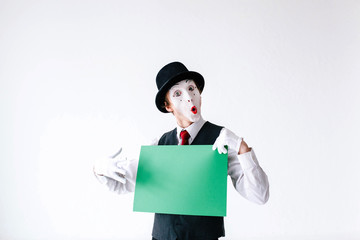 Surprised mime holds green paper in his arms