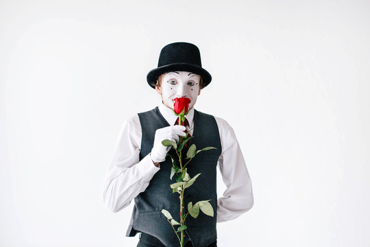 Mime in hat and waistcoat smells red rose