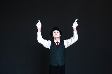 Funny mime in black hat raises his fingers up