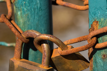 Close up on two rusty and weathered padlocks and chains holding a turquoise gate shut.