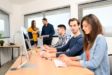 portrait of a handsome young man in high school classroom working in computer on row with teacher and classmates in background