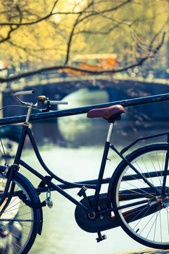 Diversity of City Transportation / Detail of vintage parking bicycle and view to next canal bridge (blurred background) with passing yellow car in Amsterdam, Holland