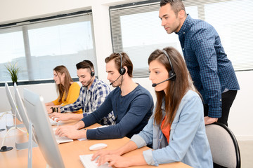 group of young people with desktop computer in row and headset training with teacher instructor in customer service call support helpline business center