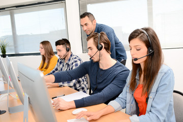 group of young people with desktop computer in row and headset training with teacher instructor in customer service call support helpline business center