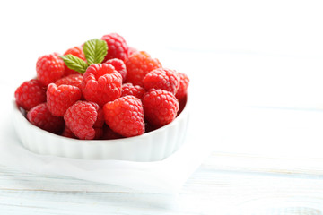 Red raspberries in bowl on a white wooden table