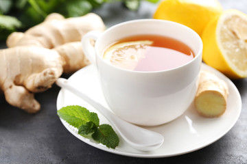 Cup of tea with ginger root and lemon on grey wooden table