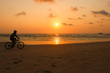 Silhouette of a man rides a bike at sunset. The men Exercise by bike riding on the beach.