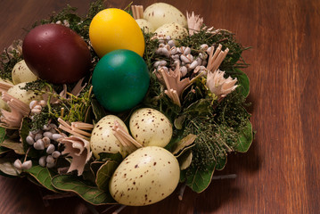 Colorful Easter eggs stacked in decorative garland on a brown table - obrazy, fototapety, plakaty