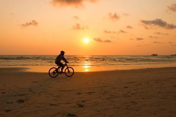 Silhouette of a man rides a bike at sunset. The men Exercise by bike riding on the beach.