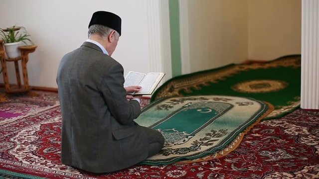 An old mullah pray holding the Koran in hands