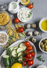 Healthy vegetarian food ingredients - pasta, zucchini, tomatoes, herbs, spices, vegan cheese, olive...