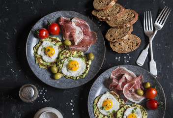 Delicious snack or appetizer - prosciutto, zucchini fritters, fried quail eggs, tomatoes, olives on a dark table, top view. Mediterranean style food. Flat lay