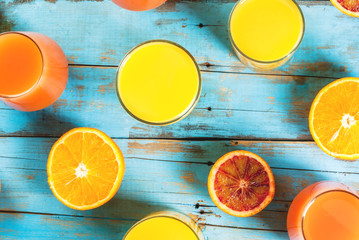 Concept of summer refreshing drink and fruits, bright colors. Glasses with juice from classic and Sicilian oranges, halves of oranges. On an old rustic blue wooden table. Top view
