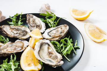 Oysters with lemon fruit on a black plate on a white wood table.