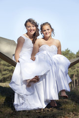 two brides in white dresses pose on hammock in forest on sunny summer day