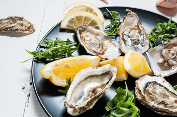 Oysters with lemon fruit on a black plate on a white wood table.