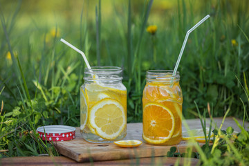 Two glass jars with lemonade on a wooden stand on the grass. Soda in a jar with a lid. Breakfast on the grass. At sunset.