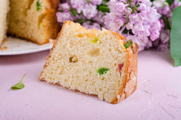 Slice of pannetone cake with cugar fruits and lilac flowers on spring background. Selective focus