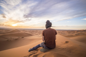 Fototapeta na wymiar A man is enjoying the sunset on the dunes in the Sahara Desert - Merzouga - Morocco