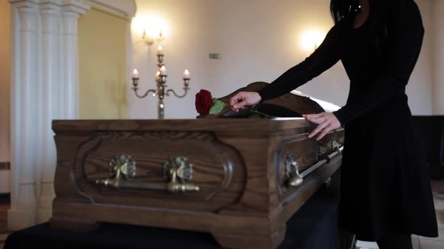 sad woman putting red rose into coffin at funeral