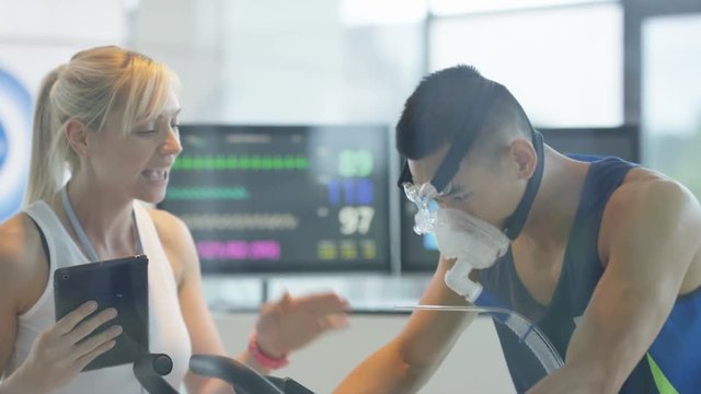  Man with breathing equipment on exercise bike having fitness levels analyzed by sports trainer. 