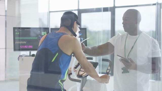  Sports professional analyzing man's fitness levels with hi tech equipment. Professional athlete in training, personal trainer at the gym or scientific research concept. 