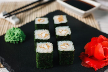 Delicious, tasty and fresh sushi rolls served on black slate with ginger and wasabi. Set of japanese maki with salmon tartar wrapped in nori, close up.