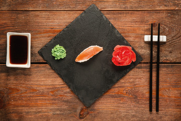 Japanese sushi background, nigiri served on black slate, on wooden rustic table, flat lay. Healthy national seafood, gourmet delicacy.