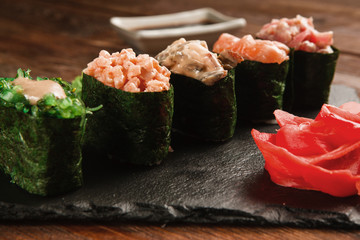 Fresh delicious set of five gunkan sushi served on black slate with ginger, closeup. Japanese...