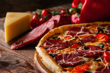 Tasty fresh italian pizza with cheese, salami sausage and cherry tomatoes served on dark wood background, close up. Fast food.