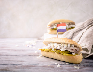 Traditional dutch snack, seafood sandwich with herring, onions and pickled cucumber. Broodje haring. Copy space. With flag of Netherlands. Retro style toned.