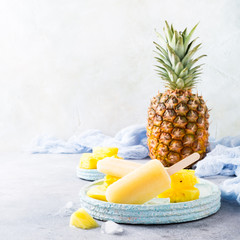 Delicious homemade pineapple popsicles on light blue plate on gray background. Summer food concept with copy space.