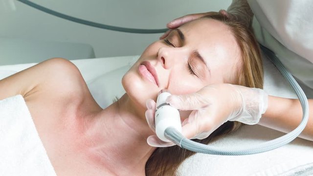 Skillful beautician treating female face by special equipment